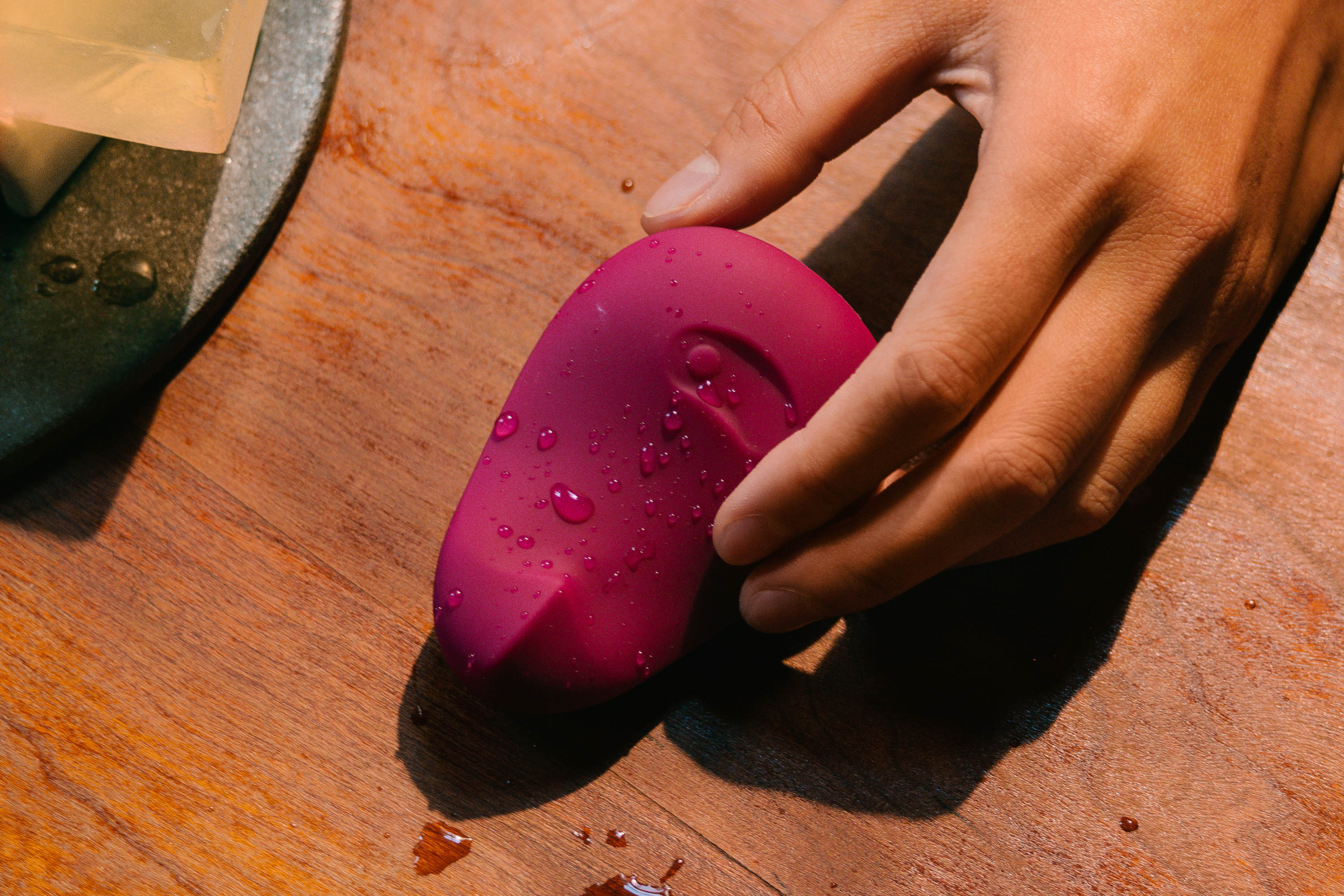 Hand holding a purple Dame sex toy on a wooden side table