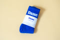 Dame Socks | A pair of bright blue Dame Socks, folded in white packaging, on beige background