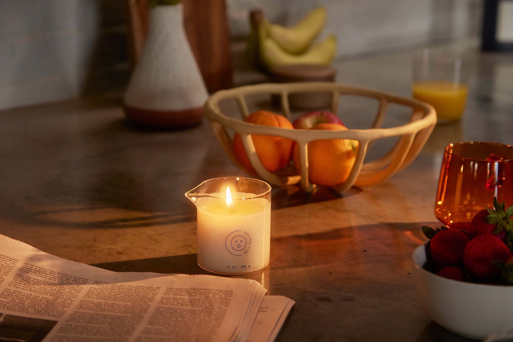 Melt Together | Dame Melt Together Massage Oil Candle Lighted on top of a dinner table next to a newspaper